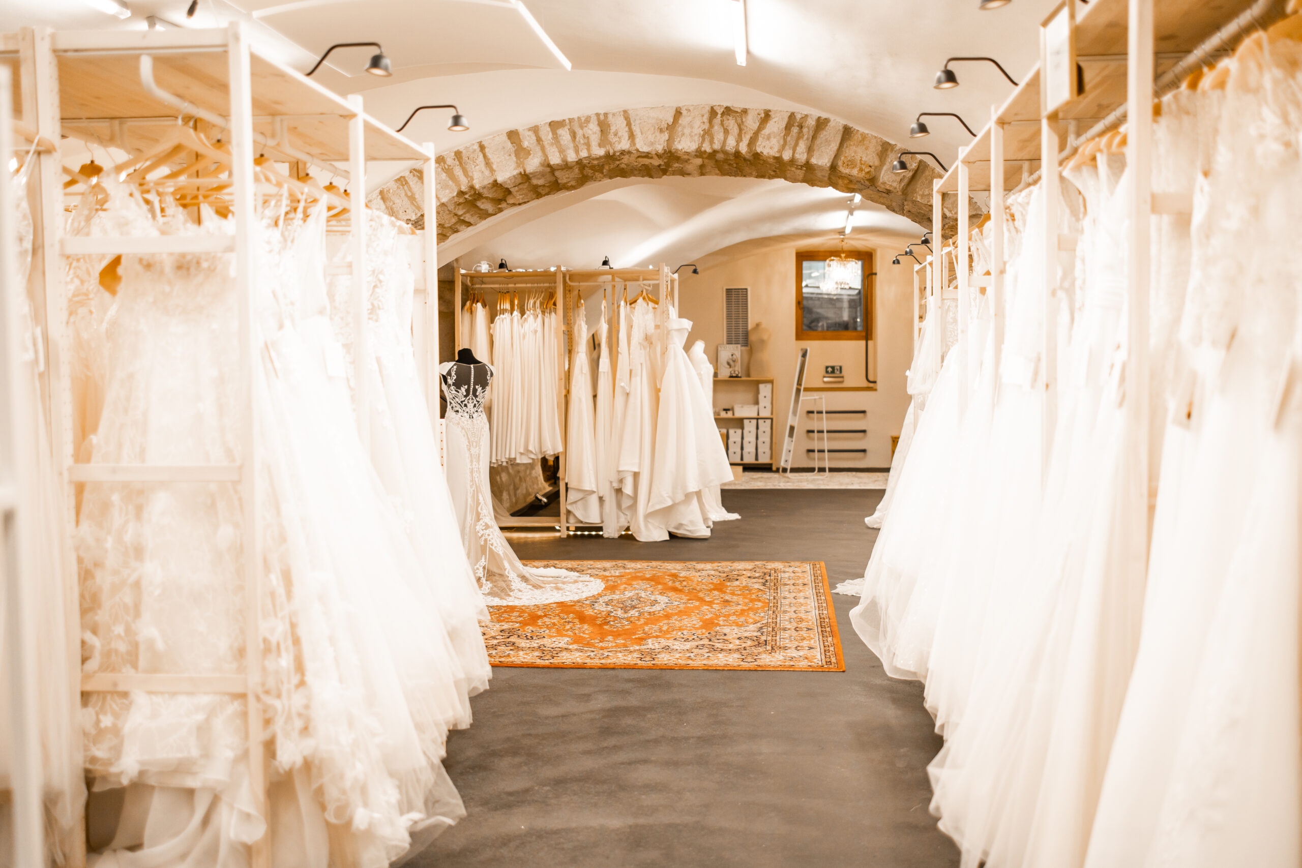 Im Vordergrund Preloved Brautkleider mit Blick durch den Torbogen auf den Anproberaum im Gewölbe. Ein alter Perserteppich leitet den Blick auf die Kleider von Lisa Dörr Couture.