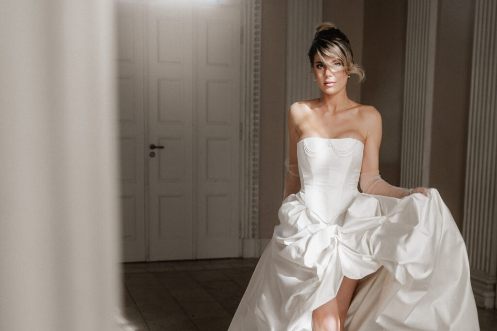 Braut im Brautkleid Winnifred, Corsagenkleid mit Perlenverzierung, Spitz zulaufender Corsage und trendigem gerafften Rock mit sichtbarem Bein, royal